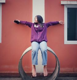 Portrait of young woman sitting against wall 