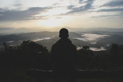 Rear view of silhouette man standing on mountain against sky