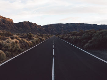 Empty road leading towards mountains against sky