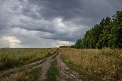 Dirt road amidst field against sky