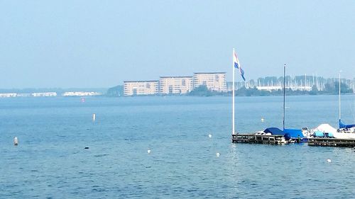 Sailboats in sea against buildings in city against clear sky