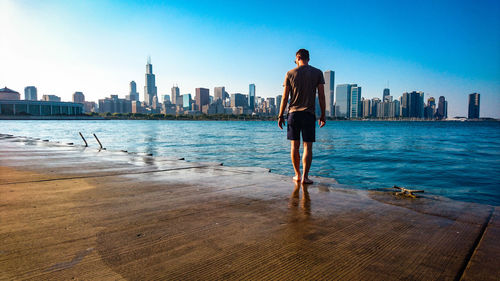 Full length of man standing on sea with city in background