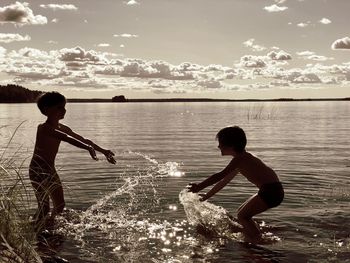 Rear view of children on sea against sky during sunset