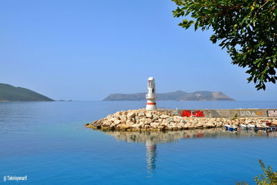 Lighthouse by sea against clear blue sky