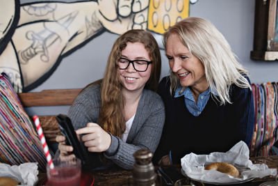 Smiling daughter showing smart phone to woman while sitting at dining table