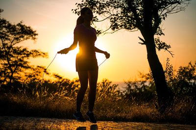 Silhouette young woman skipping on road amidst trees during sunset
