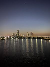 Illuminated city by sea against sky at night