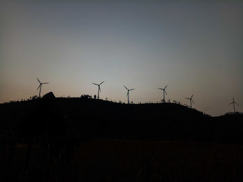 Silhouette windmill on field against sky at sunset