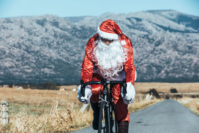 Santa claus in red costume riding modern bike along empty road in highlands on sunny day