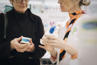 Midsection of senior customer and female owner holding medicines at pharmacy store