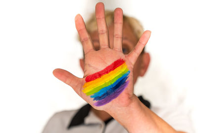 Close-up of man showing rainbow flag painting on palm against white background