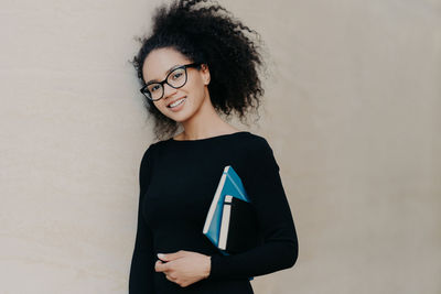 Portrait of smiling young woman standing against wall