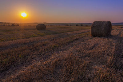 Hay bales on field against sky during sunrise