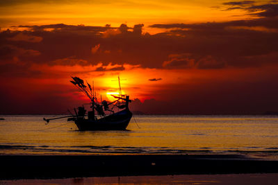 Silhouette boats moored on sea against orange sky