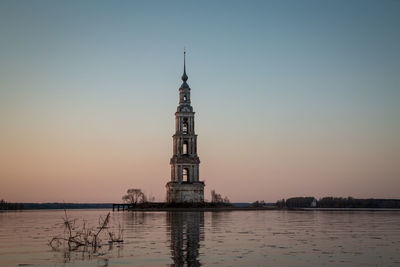 Lighthouse by sea against clear sky during sunset