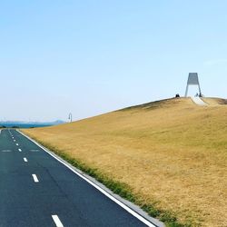 Empty road amidst field against clear sky