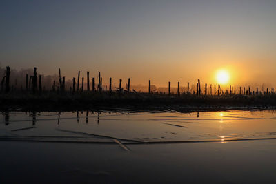 Silhouette wooden posts in lake against orange sky