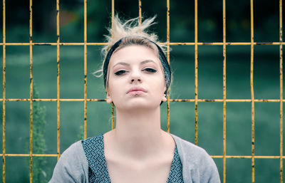 Portrait of beautiful young woman standing against fence