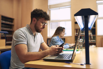 Young boy uses a mobile phone while studying at the library