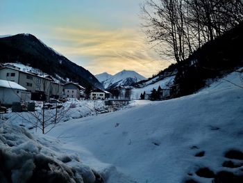Houses by snow covered mountains against sky during sunset