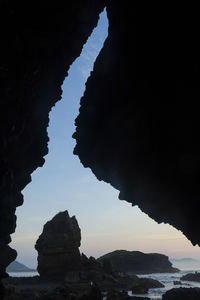Silhouette rock formations by sea against sky