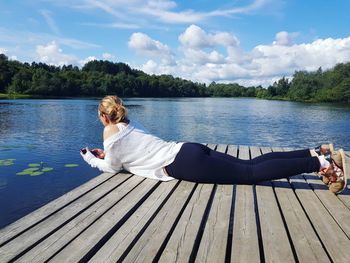 Woman sitting on pier by lake against sky