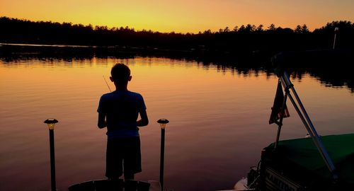 Rear view of silhouette man standing by lake against sky during sunset