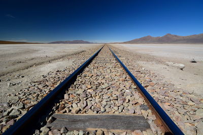 Railroad track in desert against clear blue sky