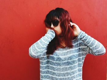 Young woman wearing sunglasses standing against red background