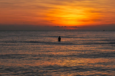 Silhouette person on sea against orange sky