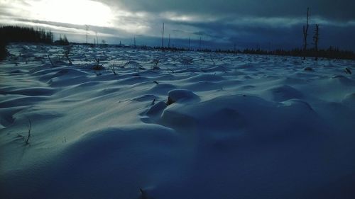 Snow covered landscape against cloudy sky