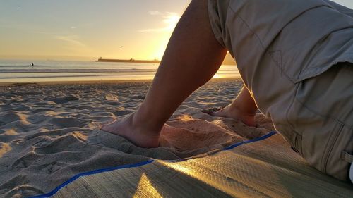 Low section of man on beach against sky during sunset