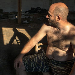 A model man sits in the dark space of an abandoned warehouse. his shadow is on the floor.