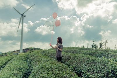 Woman standing on field with balloons against sky