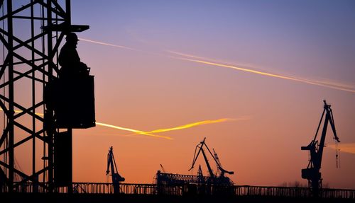 Silhouette cranes against sky during sunset