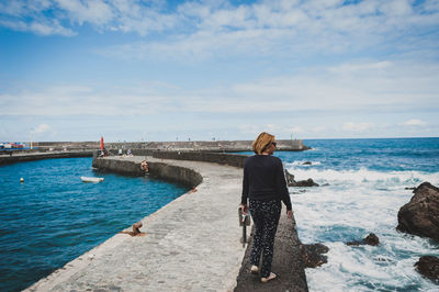 Rear view of woman walking on retaining wall at pier