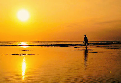 Silhouette person on beach against sky during sunset