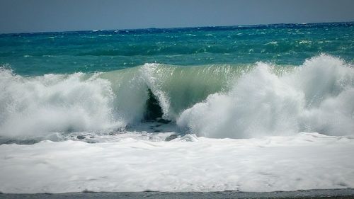 Waves splashing on shore against clear sky