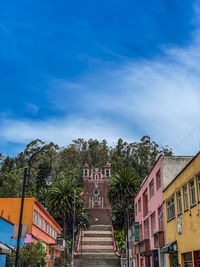 Houses and trees by building against blue sky