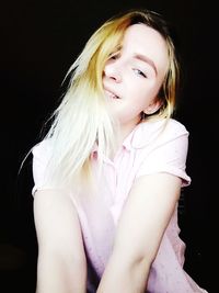 Portrait of smiling woman sitting against black background