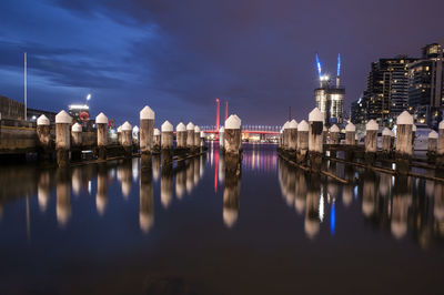 Wooden posts on river against sky in city at night