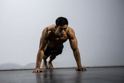 Shirtless man doing push-ups against wall