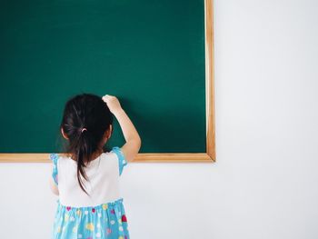 Rear view of girl writing on blackboard in classroom