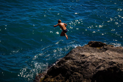 High angle view of man jumping on rock in sea