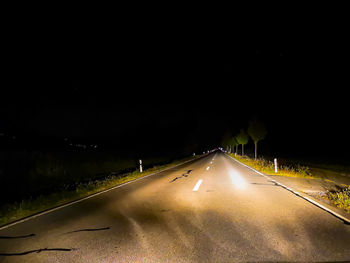 Road amidst illuminated street against sky at night