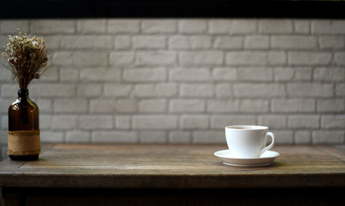 White coffee mug on a wooden table and white brick background.