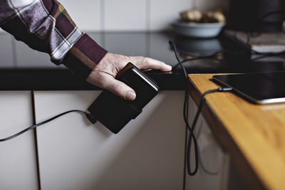 Cropped hands of senior man holding smart phone at kitchen counter