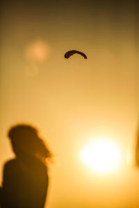 Low angle view of silhouette boy flying against sky during sunset
