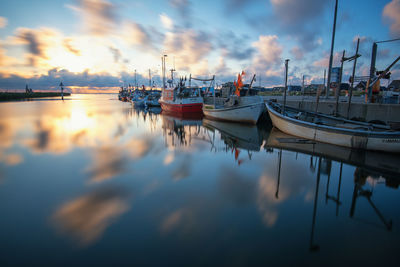 Boats moored in harbor at sunset