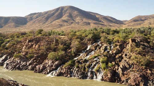 Scenic view of river flowing on arid land against sky
